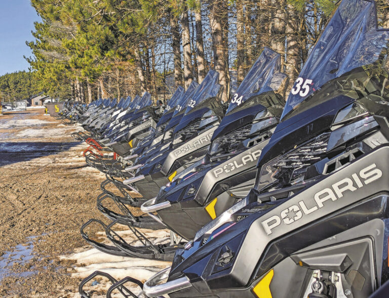 Munising Beacon Photo of a row of new Polaris rental snowmobiles sitting unused at Renze Powersports on an unusually warm February weekend.